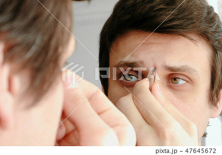 Young man plucking his eyebrows with tweezers. Styling eyebrows. 47645672