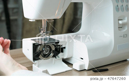 Close-up female hands test sewing machine after repair, pulling the thread. Front view. 47647260