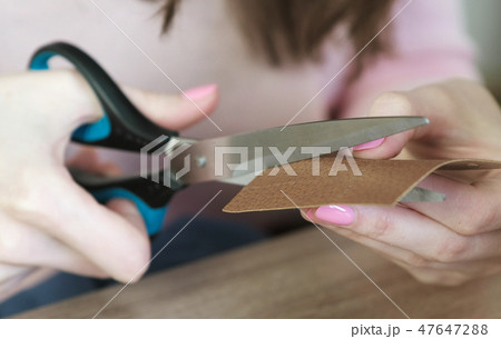Close-up of the woman's hands cut out a piece of leather, preparing for sewing, cutting. 47647288