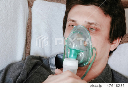 Use nebulizer and inhaler for the treatment. Young man's face inhaling through inhaler mask lying on Use nebulizer and inhaler for the treatment. Young man's face inhaling through inhaler mask lying on 47648285