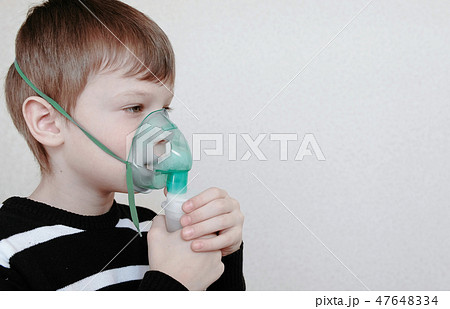 Use nebulizer and inhaler for the treatment. Boy inhaling through inhaler mask. Side view. 47648334