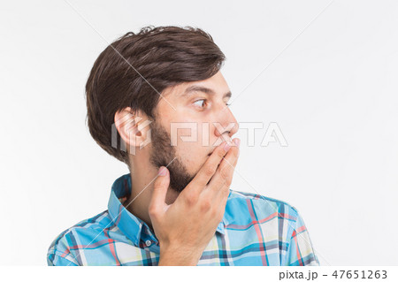 People, emotions and gesture concept - young surprised man covering his mouth with his hand on white 47651263