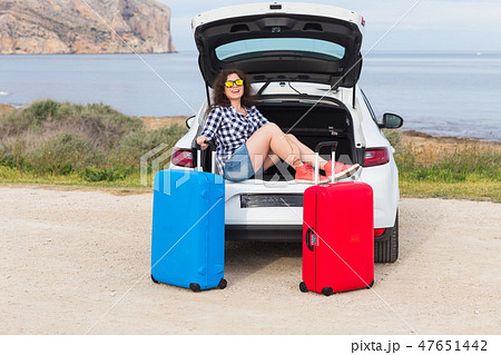 Young woman sitting in back of car smiling and getting ready to go. Girl sitting in the open trunk 47651442