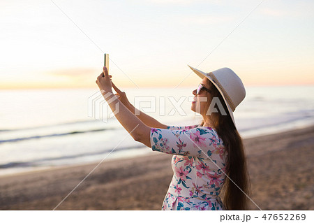 Traveler young woman is shooting video of beautiful sunset landscape on mobile phone camera. Summer Traveler young woman is shooting video of beautiful sunset landscape on mobile phone camera. Summer 47652269