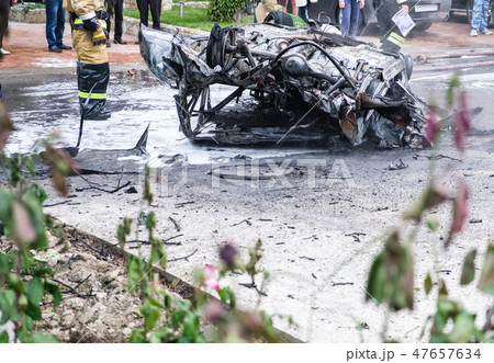 Burned car after an accident on the road. Firefighters standing nearby. Reportage picture in street. 47657634