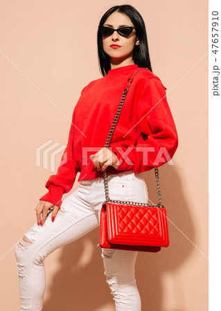 Fashion young woman in white jeans and sweater with red bag clutch in hands Fashion young woman in white jeans and sweater with red bag clutch in hands 47657910