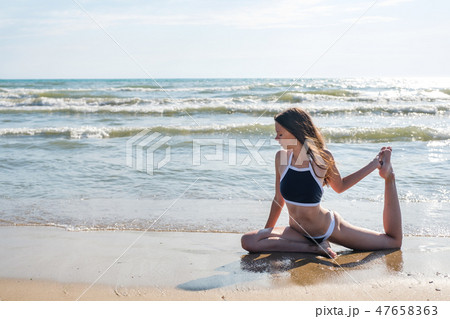 Woman in bikini practice yoga Eka Pada Rajakapotasana Royal pigeon Pose at seaside. 47658363