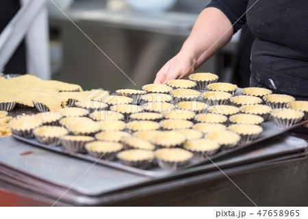Pastry chef making tartlets, putting the dough in baking dishes, at kitchen of pastry shop. 47658965