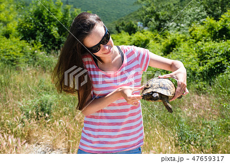 Close-up woman brunette in sunglasses and striped t-shirt keeping turtle in her hands in the forest Close-up woman brunette in sunglasses and striped t-shirt keeping turtle in her hands in the forest 47659317