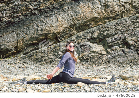 Side view of a healthy mature woman figure stretching and exercising on a rock platform 47660028