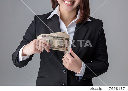 スーツの女性が何十万のお金を手に入れてスーツの懐に入れようとし喜んでいるとしている場面 スーツの女性が何十万のお金を手に入れてスーツの懐に入れようとし喜んでいるとしている場面 47668137