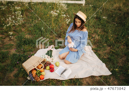 Charming pregnant woman sits in te fieln on the plaid. Woman dressed in blue dress and knitted hat 47673842