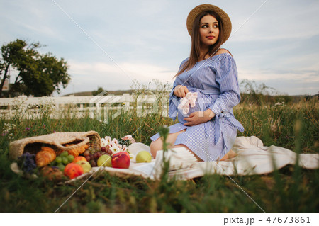 Charming pregnant woman sits in te fieln on the plaid. Woman dressed in blue dress and knitted hat 47673861
