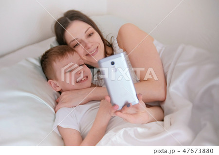 Mom and son take selfie on her mobile phone. Morning in bed. Mom and son take selfie on her mobile phone. Morning in bed. 47673880