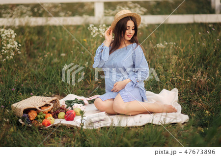 Young pregnant woman sitting in the field and relax. She took a fruit basket. Summer 47673896