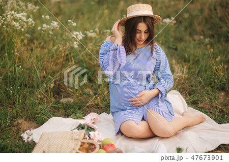 Young pregnant woman sitting in the field and relax. She took a fruit basket. Summer 47673901