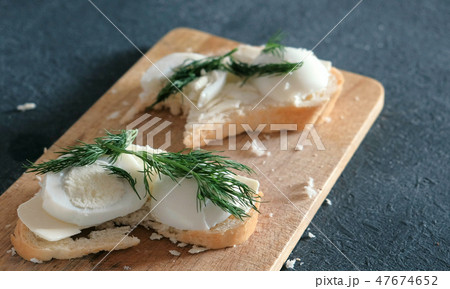 Closeup sandwiches with bread, butter, eggs and dill on wooden board in black background. Making a 47674652