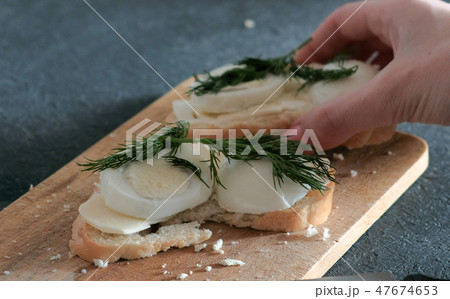 Closeup woman's hand takes a sandwich with bread, butter, eggs and dill from wooden board. 47674653