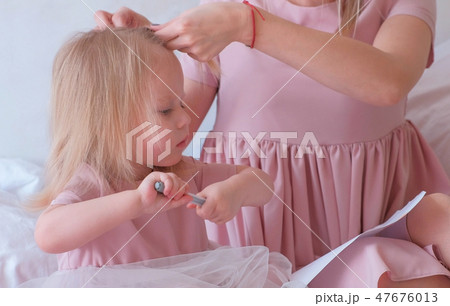 Mom braids hair to her little charming daughter in pink dresses while she painting with felt-pen. 47676013