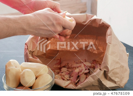 Man's hands peeling potatoes. Paper bag with cleaning of the potatoes. Potatoes in bowl 47678109