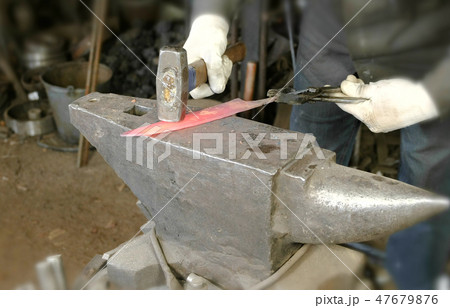 Making the knife out of metal at the forge. Close up blacksmith's hands hitting hot metal with a 47679876