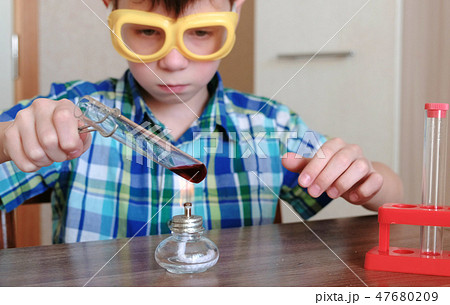 Experiments on chemistry at home. Boy heats the test tube with red liquid on burning alcohol lamp. 47680209