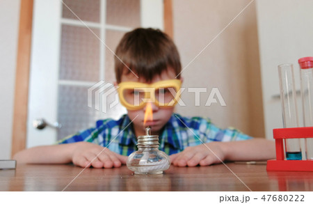 Experiments on chemistry at home. Boy is looking at the burning alcohol lamp on fire with a match. 47680222