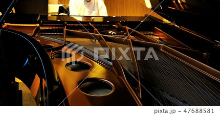 グランドピアノを弾く男性と暗がりに浮かぶミュージックワイヤー 47688581