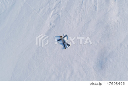 Woman makes snow angel laying in the snow. Top view. Aerial foto. Woman makes snow angel laying in the snow. Top view. Aerial foto. 47693496