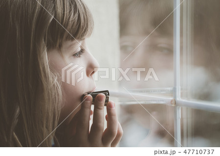 Sad girl playing harmonica by the window Sad girl playing harmonica by the window 47710737