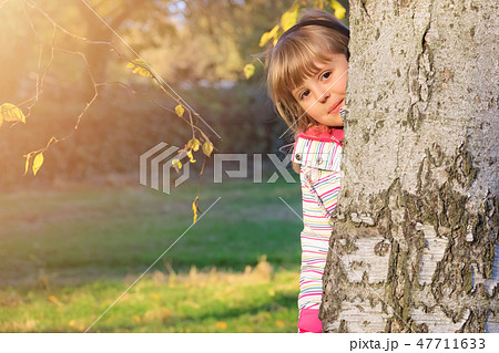 Cute little girl hiding behind a tree 47711633