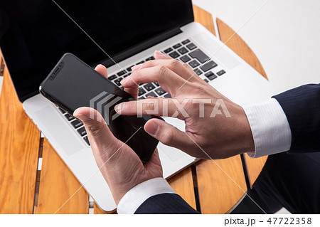 机でスーツの男性が手元アップでスマホとパソコンで仕事をしている 47722358