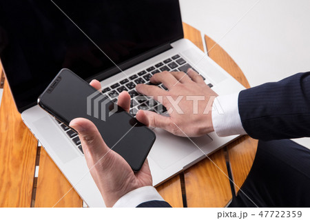 机でスーツの男性が手元アップでスマホとパソコンで仕事をしている 机でスーツの男性が手元アップでスマホとパソコンで仕事をしている 47722359