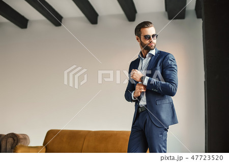 Fashion portrait of young bearded businessman in classic suit and dark sunglasses who is standing in 47723520