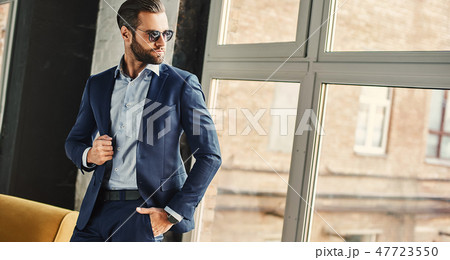 Confident and stylish. Businessman in sunglasses and fashion suit is thoughtfully looking in window Confident and stylish. Businessman in sunglasses and fashion suit is thoughtfully looking in window 47723550