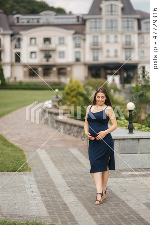 Pregnant woman in dress holds hands on belly 47729316