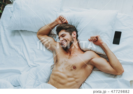 Happy young guy stretching in bed at home Happy young guy stretching in bed at home 47729882