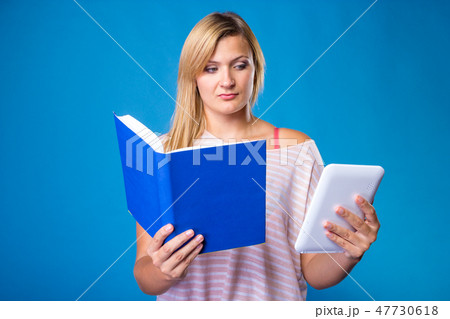 Blonde woman choosing between book and tablet 47730618
