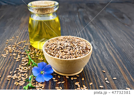 Flaxen brown seed in bowl with oil on dark board Flaxen brown seed in bowl with oil on dark board 47732381