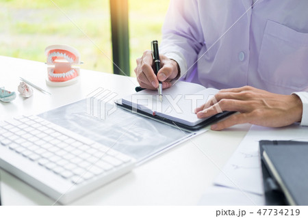 Concentrated dentist sitting at table with jaw samples tooth mod Concentrated dentist sitting at table with jaw samples tooth mod 47734219