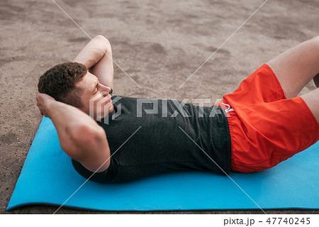 Young guy on rug. Trains twisting, abdominal muscles. Strengthening abdominal muscles. Raise torso Young guy on rug. Trains twisting, abdominal muscles. Strengthening abdominal muscles. Raise torso 47740245