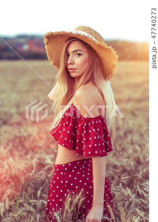 Girl in a wheat field in summer in red dress and straw hat. A woman walks across the field, long Girl in a wheat field in summer in red dress and straw hat. A woman walks across the field, long 47740273