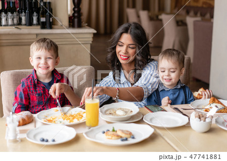 Beautiful young woman with her baby sons. Light breakfast near window in a cafe. Croissants, omelet 47741881