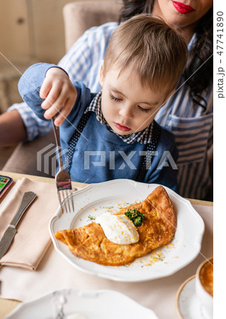 Beautiful young woman with baby son. Light breakfast near window in a cafe. Croissants, omelet 47741890