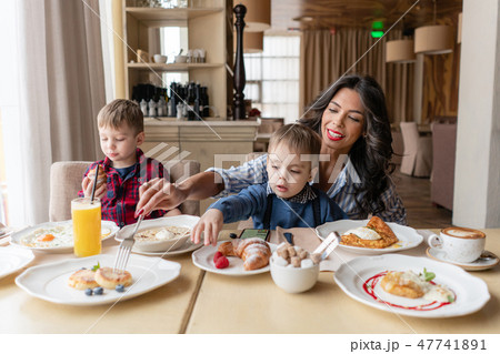 Beautiful young woman with her baby sons. Light breakfast near window in a cafe. Croissants, omelet 47741891