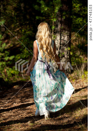 Young beautiful blonde woman in white dress with blue and green flowers posing in forest 47748103