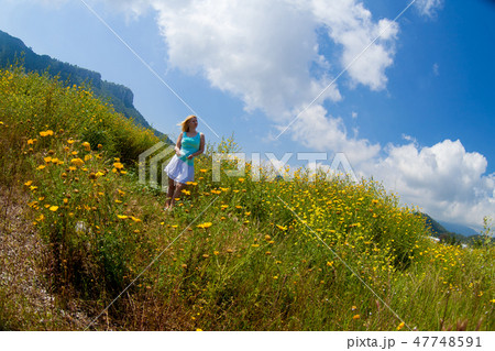 Young beautiful blonde girl in a chamomile field stands posing with a flower in her hands 47748591
