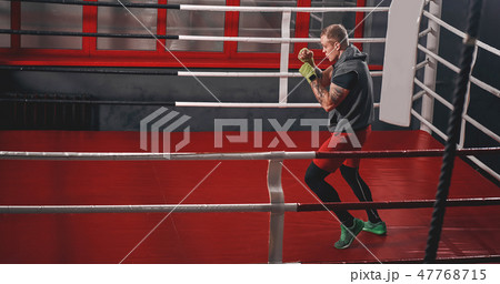 Training his boxing skills. Muscular tattooed boxer in sports clothing punching on red boxing ring Training his boxing skills. Muscular tattooed boxer in sports clothing punching on red boxing ring 47768715