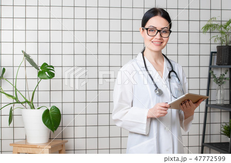 Beautiful smiling doctor wearinbg glasses standing in her modern office Beautiful smiling doctor wearinbg glasses standing in her modern office 47772599