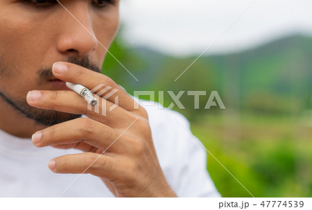 Young man smoking cigarette in the outdoors. 47774539